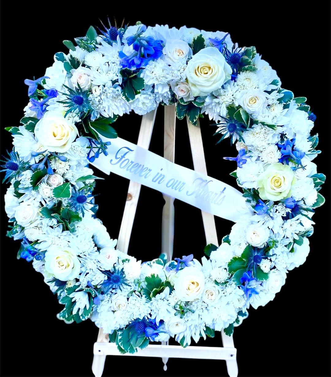 Heart-shaped floral wreath with white and blue flowers on a stand