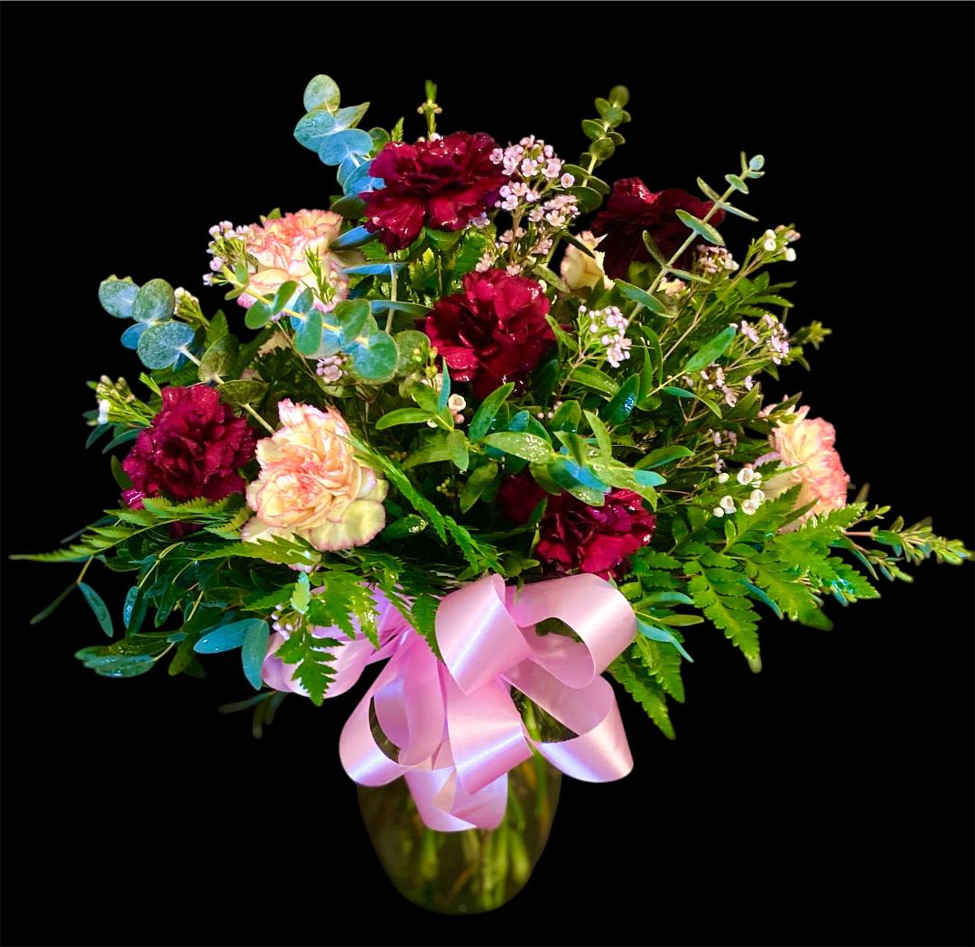 Bouquet of burgundy and blush carnations in a glass vase with a pink ribbon