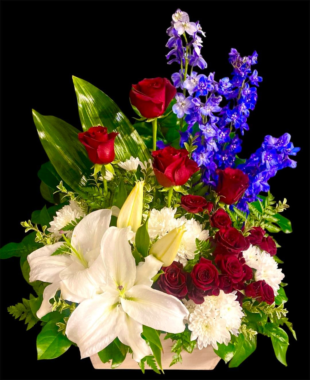 Bouquet of red roses, white lilies, and blue flowers in a low container