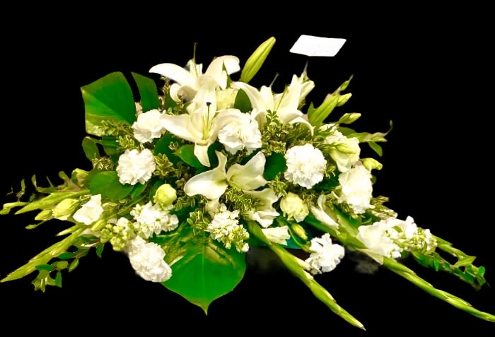 White lilies and carnations arranged with broad green leaves