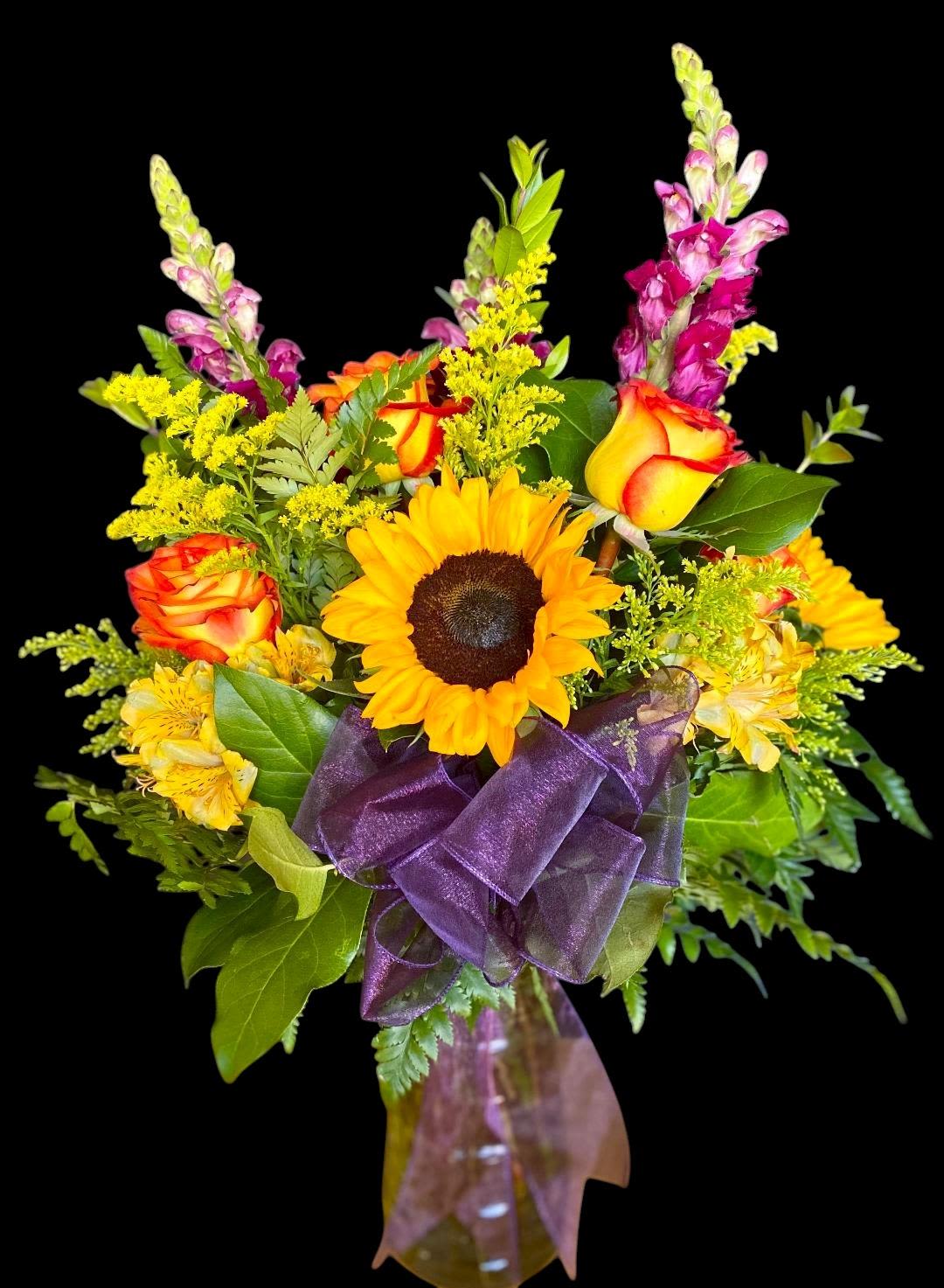 Bouquet of sunflowers, orange roses, and purple snapdragons in a glass vase