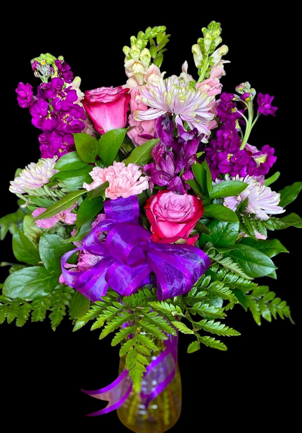 Bouquet of pink and purple flowers with a purple ribbon in a vase