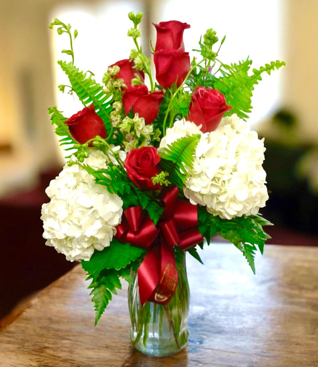 Red roses and white hydrangeas in a glass vase with a red ribbon
