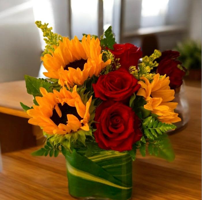 Sunflowers and red roses arranged in a green glass vase
