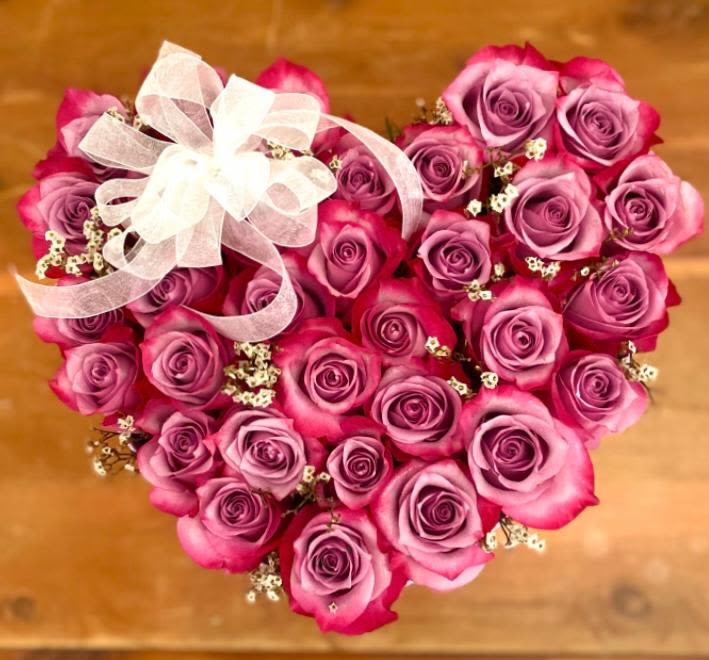 Heart-shaped bouquet of pink and purple roses with a white ribbon bow