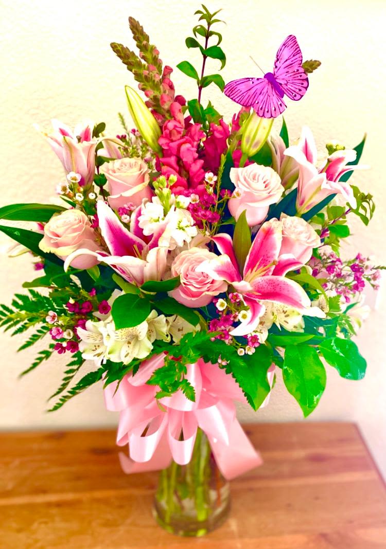 Pink roses and lilies in a glass vase with a pink ribbon and butterfly pick