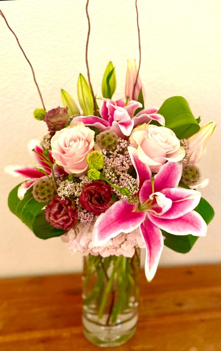 Pink lilies and roses arranged in a clear glass vase