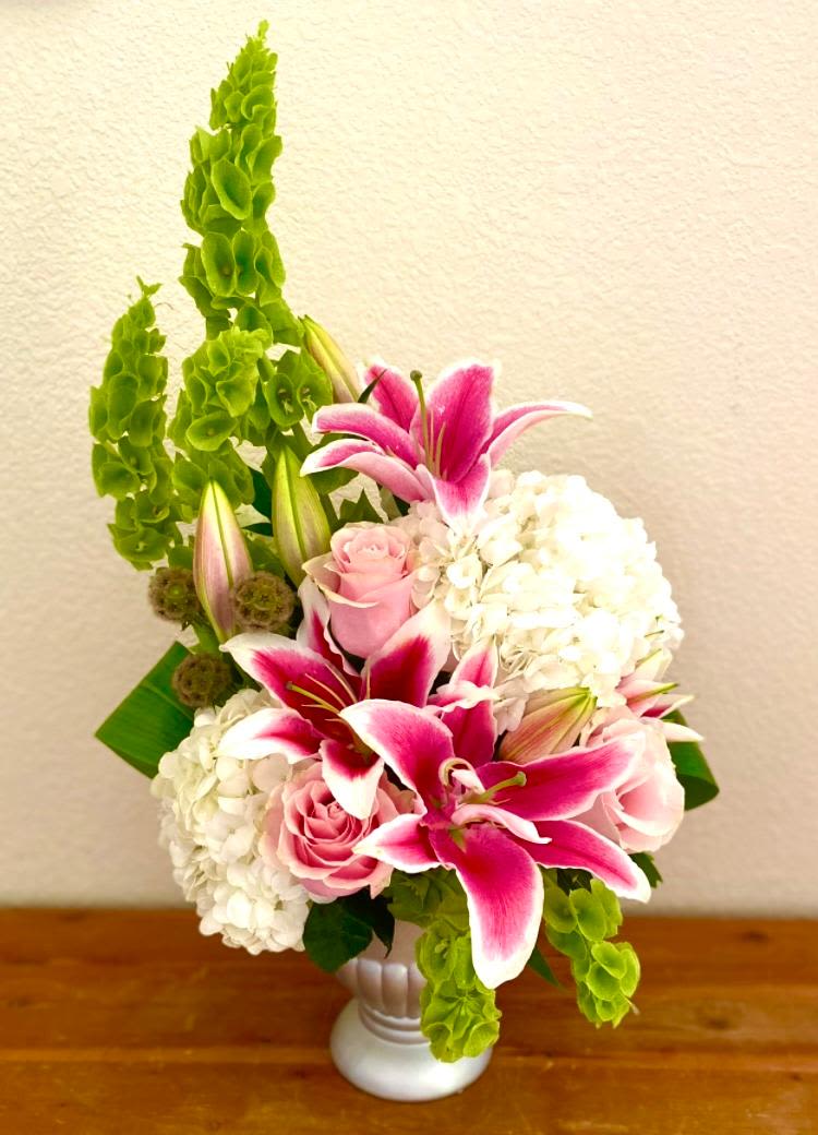 Pink lilies and roses arranged with white hydrangeas in a white vase