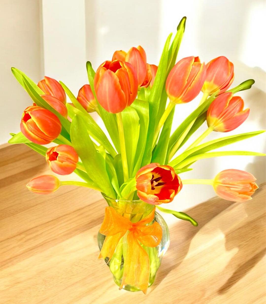 Orange tulips in a glass vase with an orange ribbon