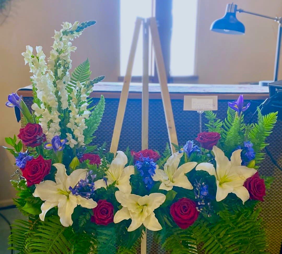 Floral arrangement with white lilies, red roses, and purple blooms on an easel