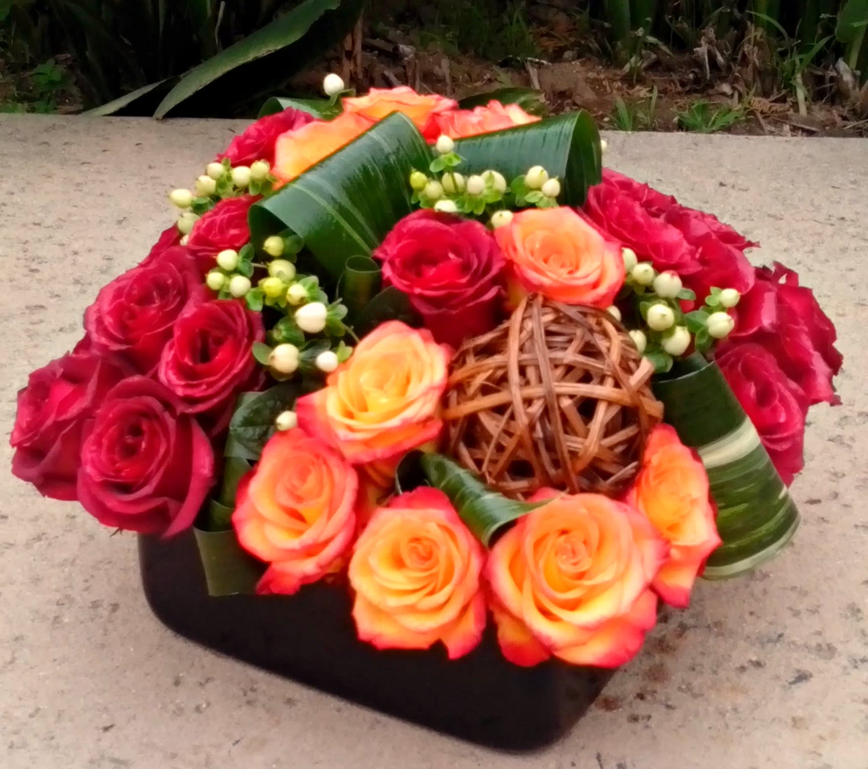 Red and orange roses arranged in a low black container with woven accents