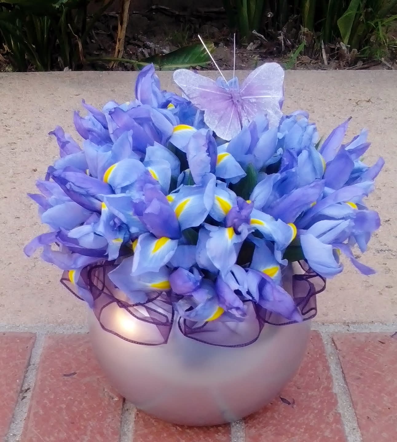 Purple iris bouquet in a round vase with a sheer ribbon and butterfly decoration