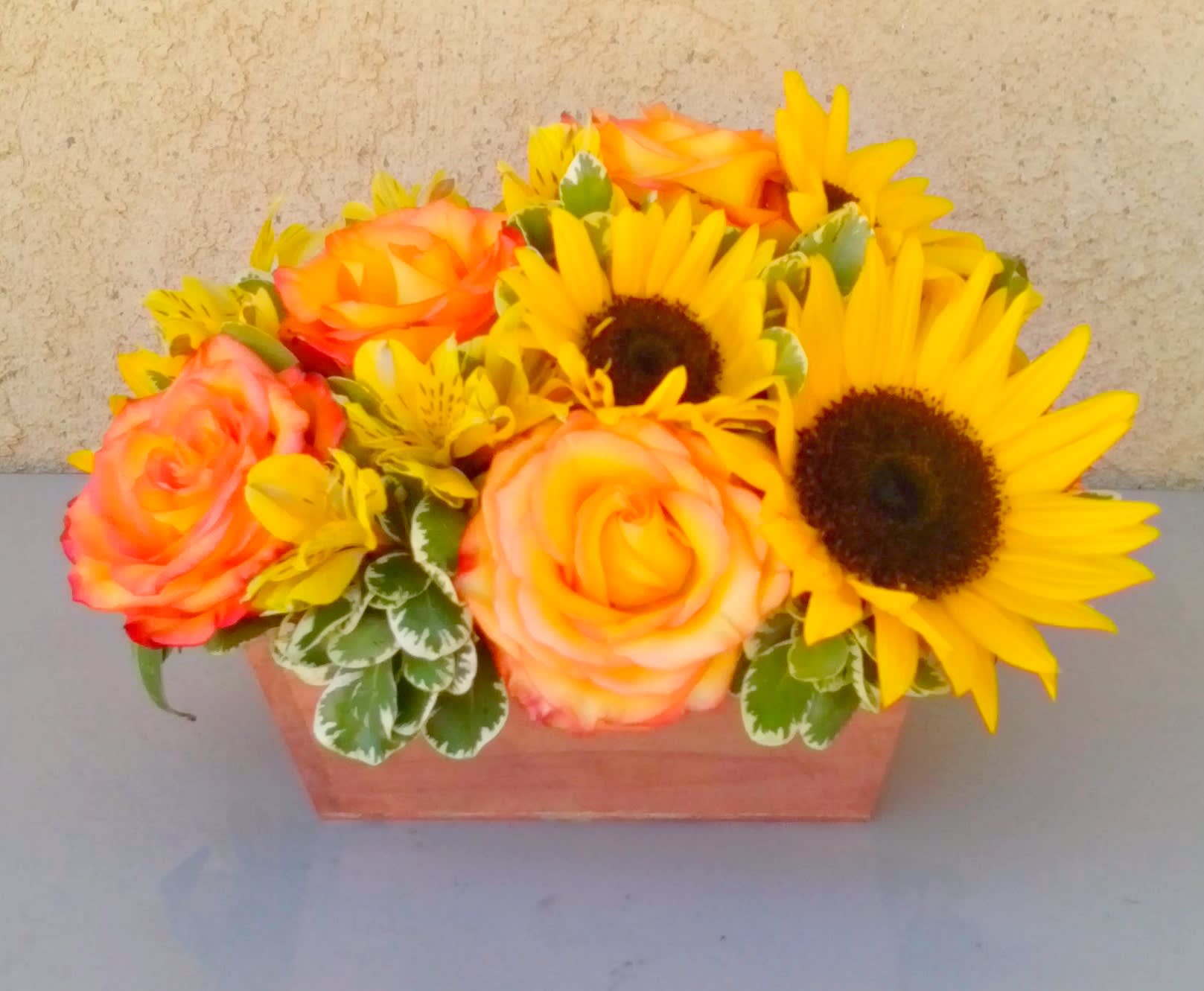 Orange roses and yellow sunflowers in a rectangular wooden container