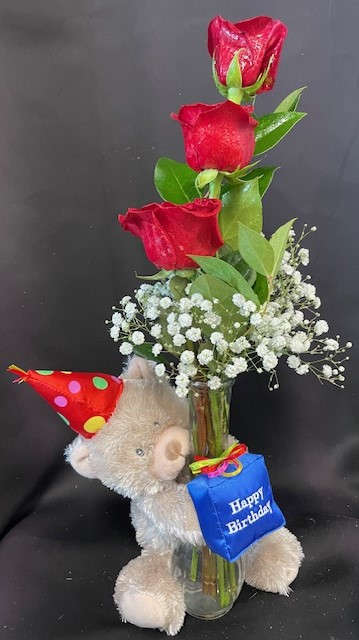Red roses in a glass vase with a teddy bear and birthday tag