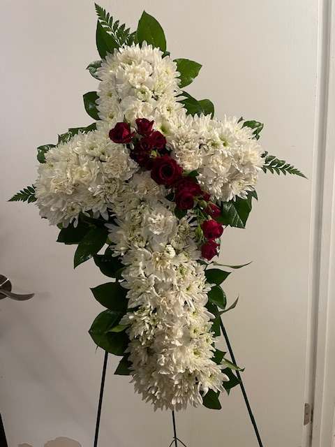 White floral cross arrangement with red roses on a stand