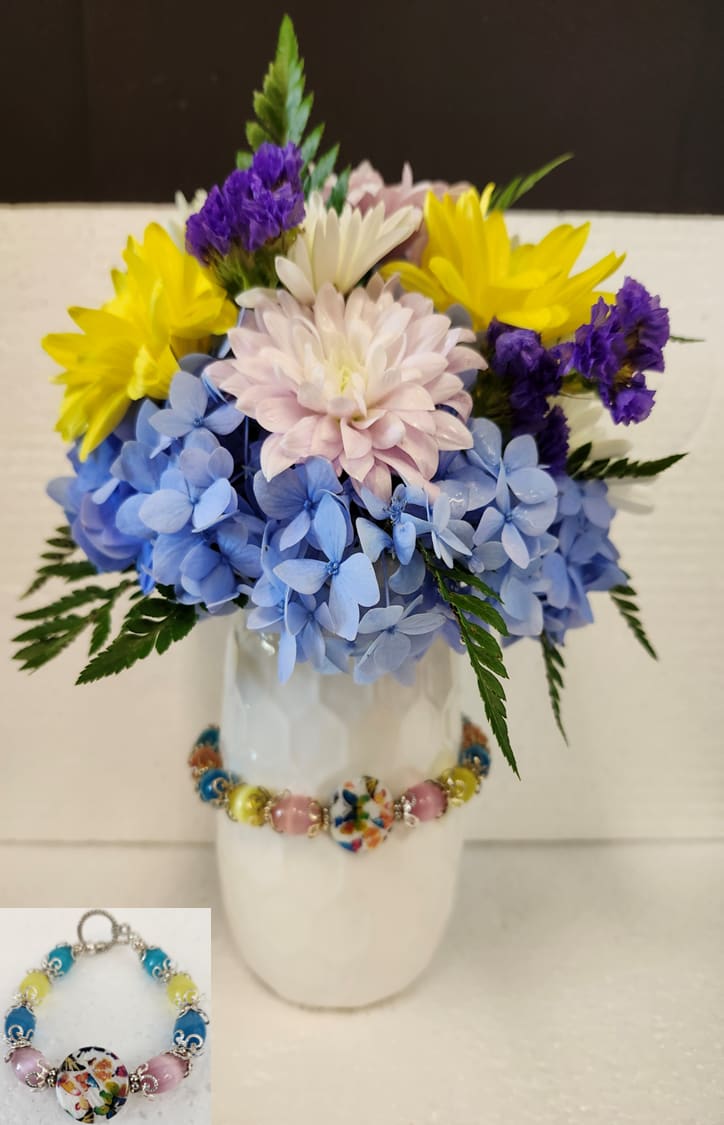 Colorful bouquet in a white vase with blue, yellow, purple, and pale pink flowers.