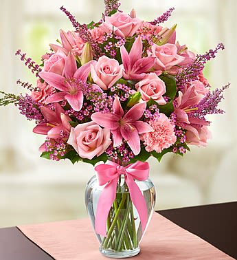 Pink roses and lilies arranged in a clear glass vase with a pink ribbon