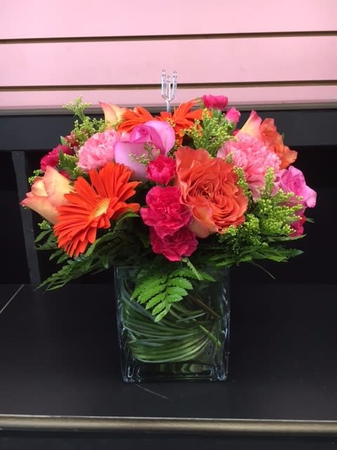Bright Mixed Bouquet in a Cube Vase - A mix of beautiful bright flowers hand-crafted and designed in a clear glass cube with long grass elegantly adding a touch of elegance to the bouquet. Roses, Gerbera, and many more flowers create a wonderful modern twist to an old favorite. It's great for any occasion, and is appropriate as a centerpiece for parties.