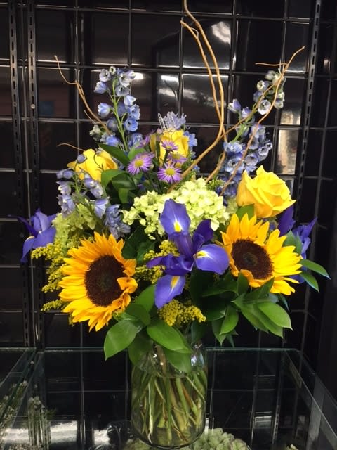 Autumn Beauty - A stunning display of fresh Autumn flowers hand-crafted and designed in a clear glass vase. Includes everyone's favorite sunflowers, hydrangea, and much more! Makes for a great gift for a loved one during the Autumn Season, or it can even be used as a centerpiece for parties.