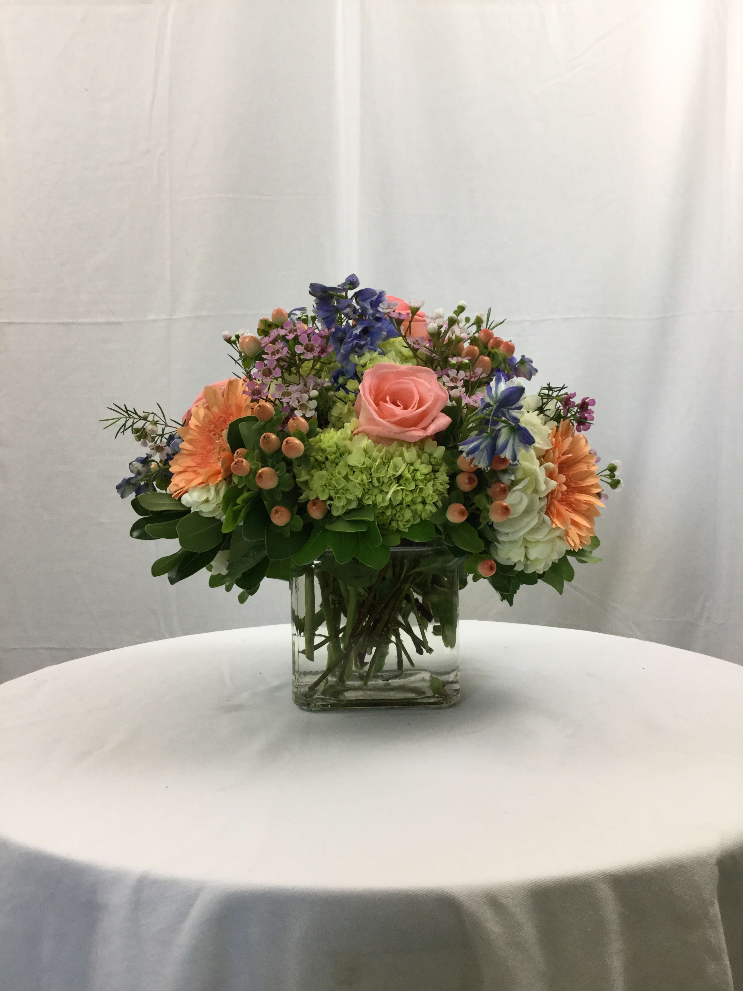 Summer Passion Centerpiece - This beautiful cube bouquet makes for the perfect centerpiece for parties, dinners or even Weddings! Each bloom compliments the other and creates a perfect marriage of flowers. Handcrafted and designed in a clear glass cube vase.