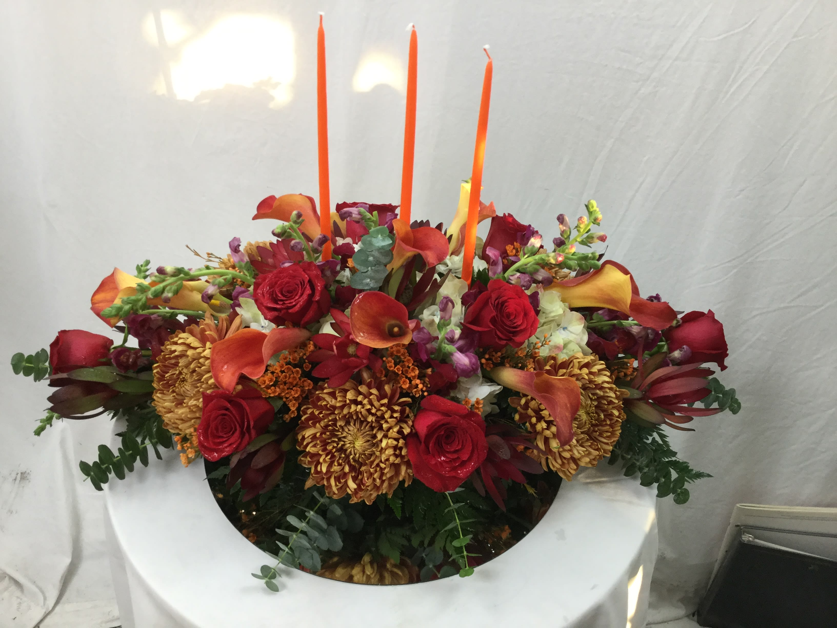 Thanksgiving Day Centerpiece - This beautiful centerpiece makes for a wonderful Thanksgiving gift. Full of Autumn blooms, fresh greens and 3 candles.