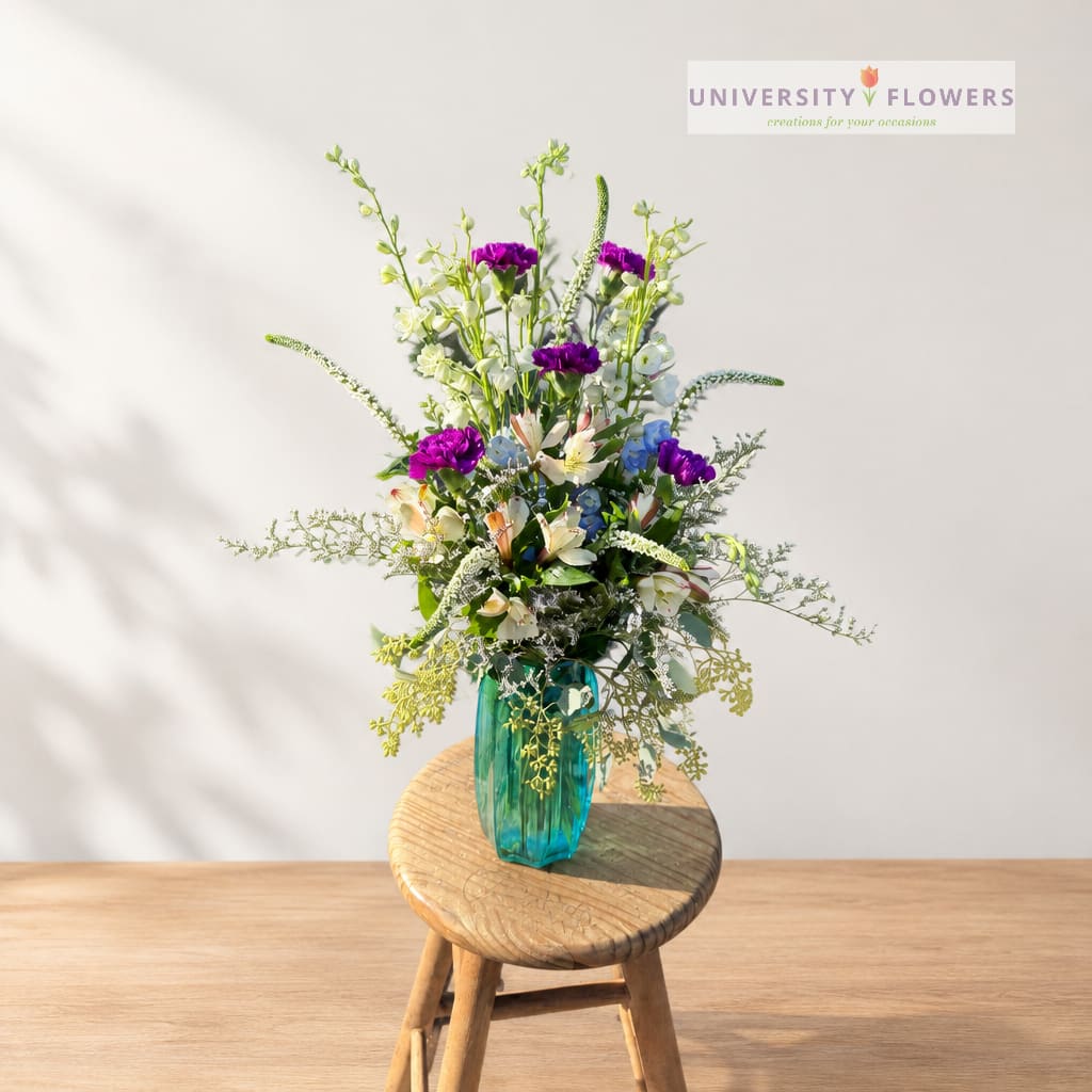 Mixed bouquet in a turquoise glass vase on a wooden stool