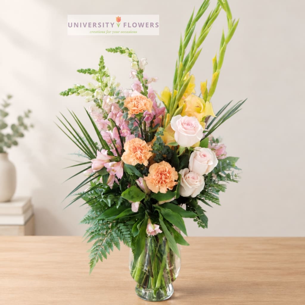 Tall mixed bouquet in a clear glass vase with pink, peach, yellow, and white flowers