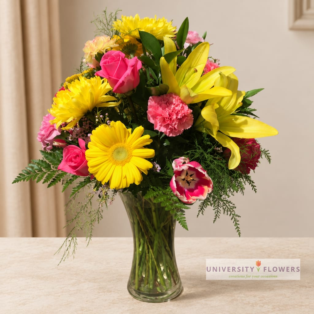 Mixed bouquet of yellow lilies, pink roses, and daisies in a glass vase