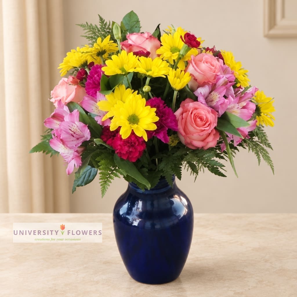 Mixed bouquet of pink roses, yellow daisies, and pink alstroemeria in a blue vase