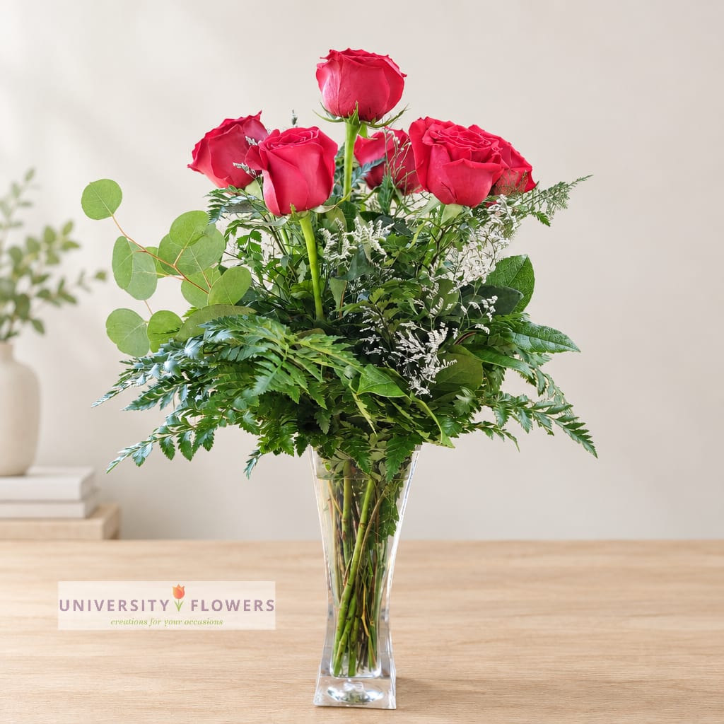 Red roses in a clear glass vase with lush greenery