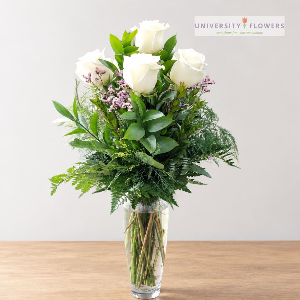 White roses in a clear glass vase with greenery and small purple filler flowers