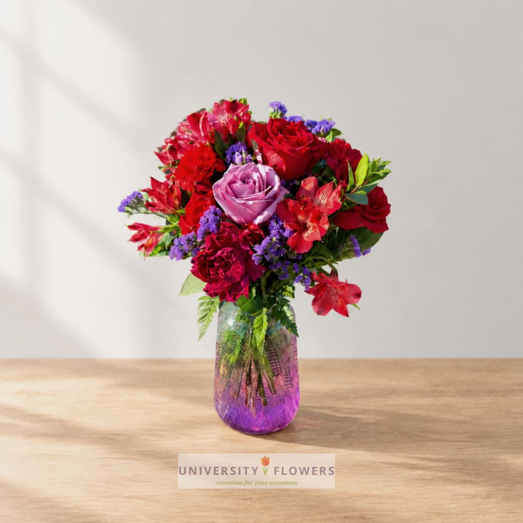 Mixed bouquet of red, pink, and purple flowers in a glass vase