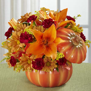 Orange and red floral arrangement in a pumpkin-shaped container