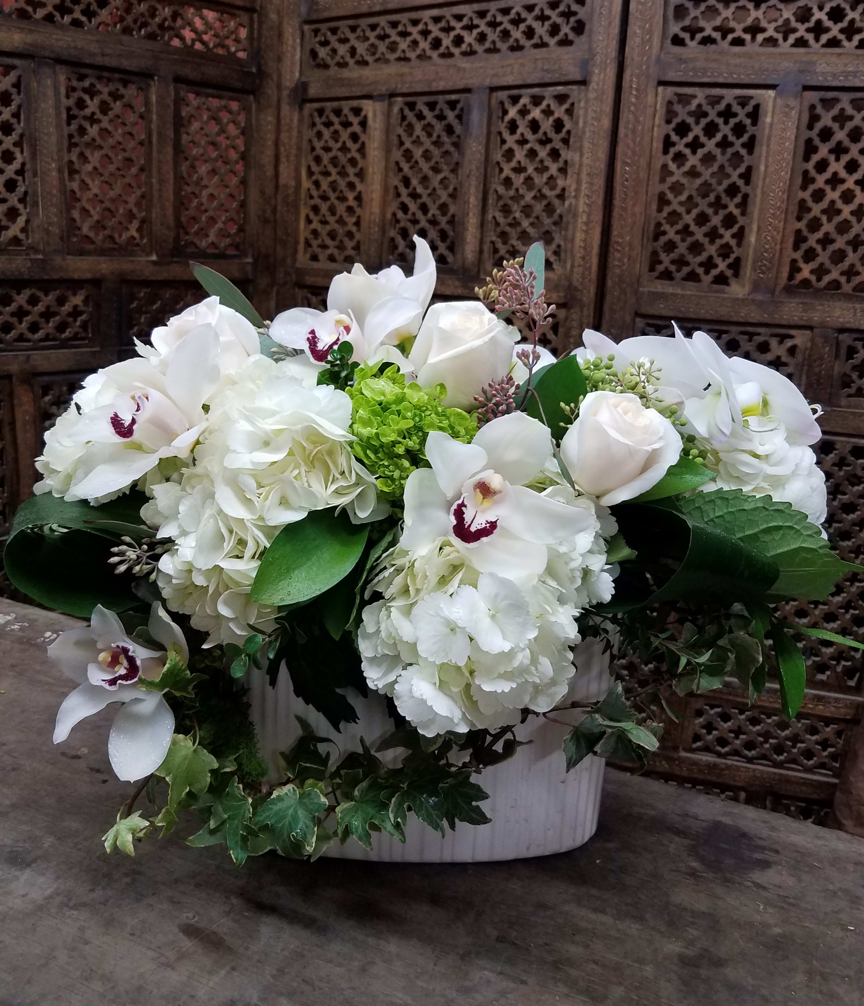 White floral arrangement in a white container with orchids and roses
