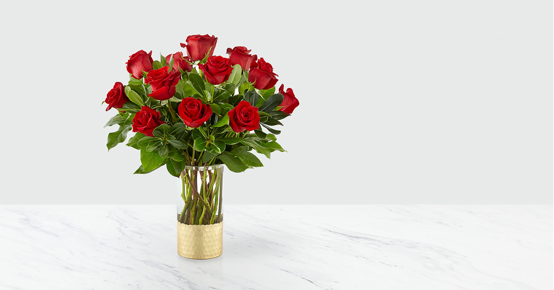 Red roses arranged in a clear glass vase with a gold base