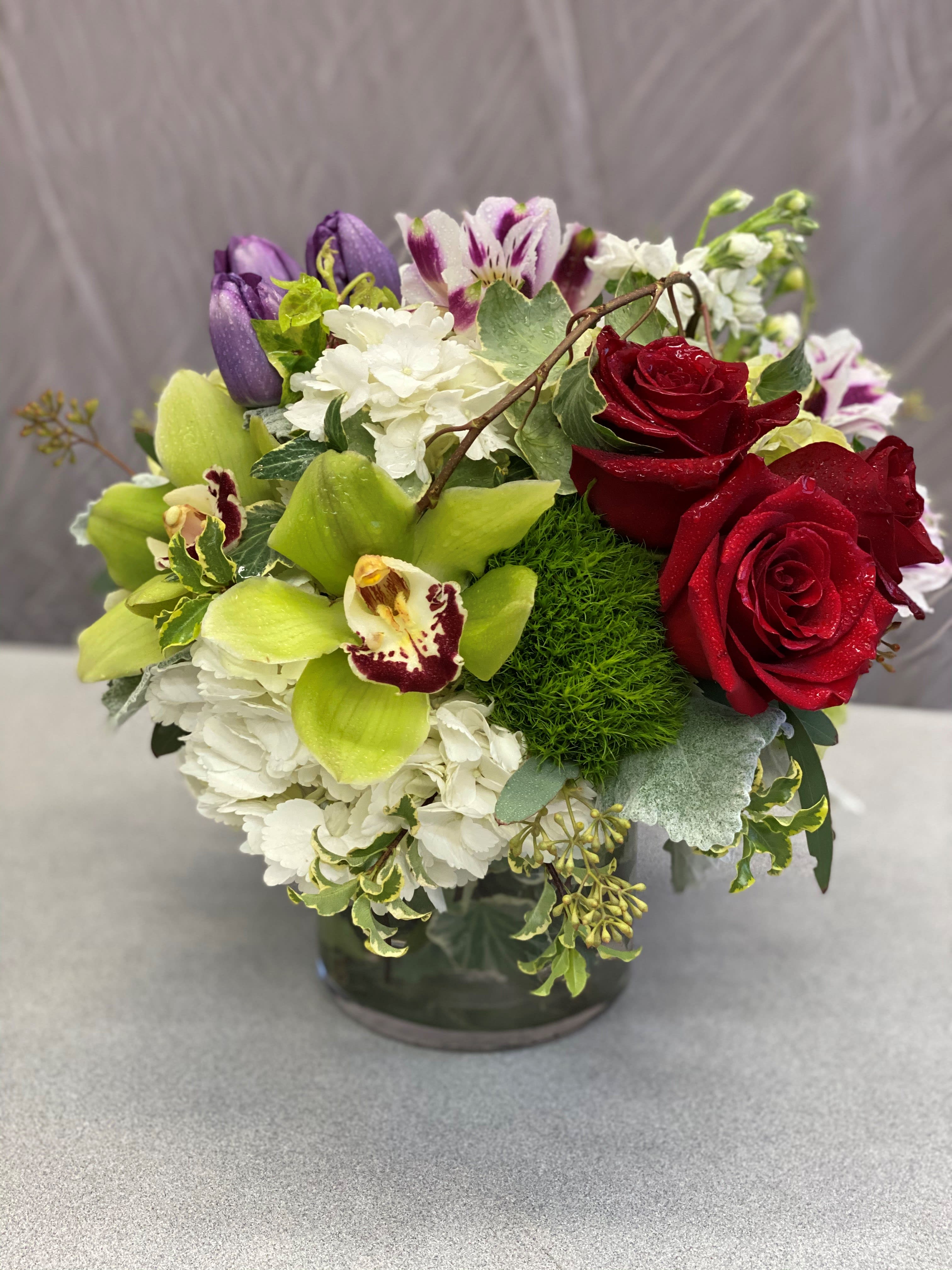 Mixed bouquet of red roses, white hydrangea, and purple orchids in a glass vase