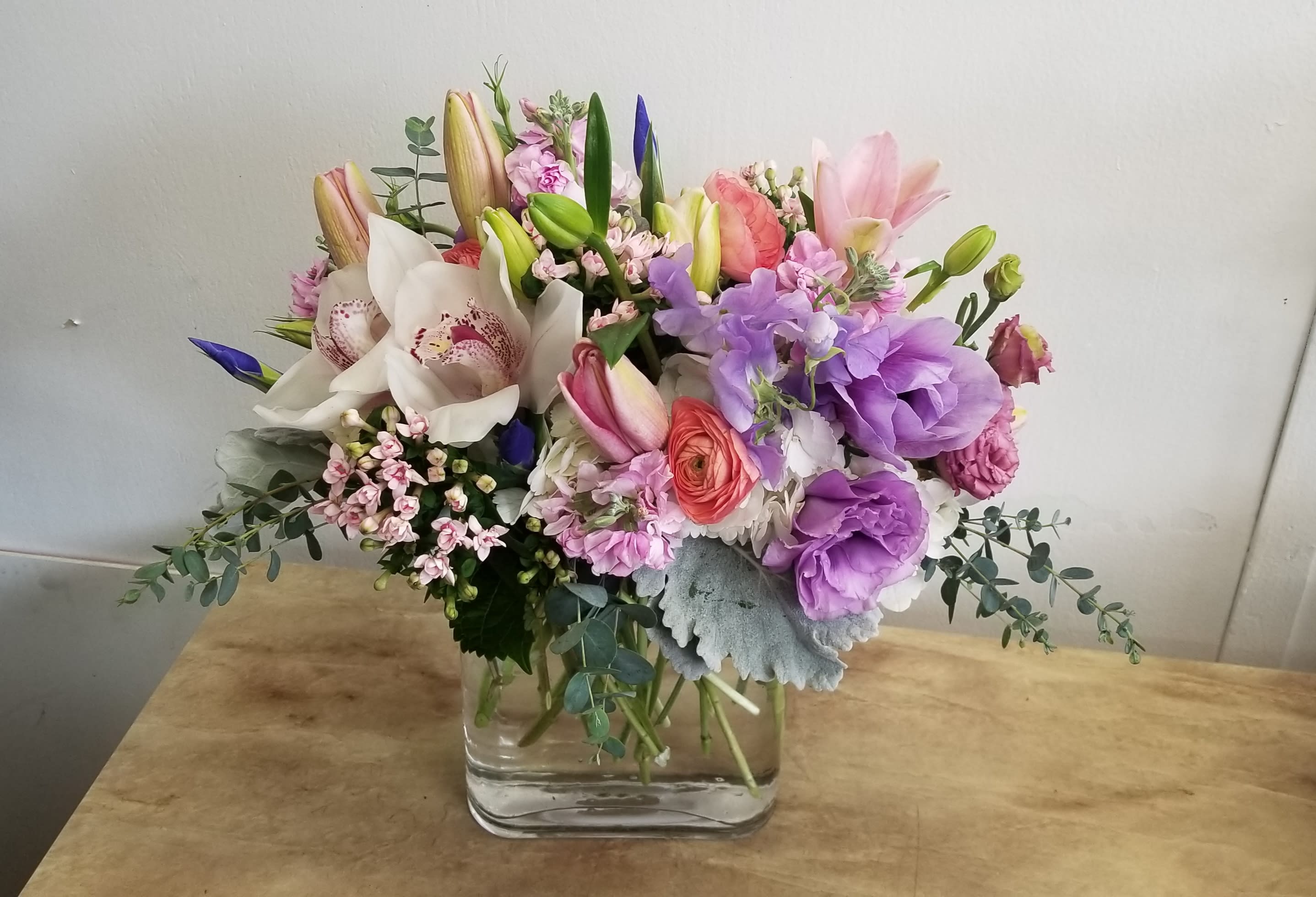 Mixed bouquet of lilies, orchids, and purple blooms in a glass vase