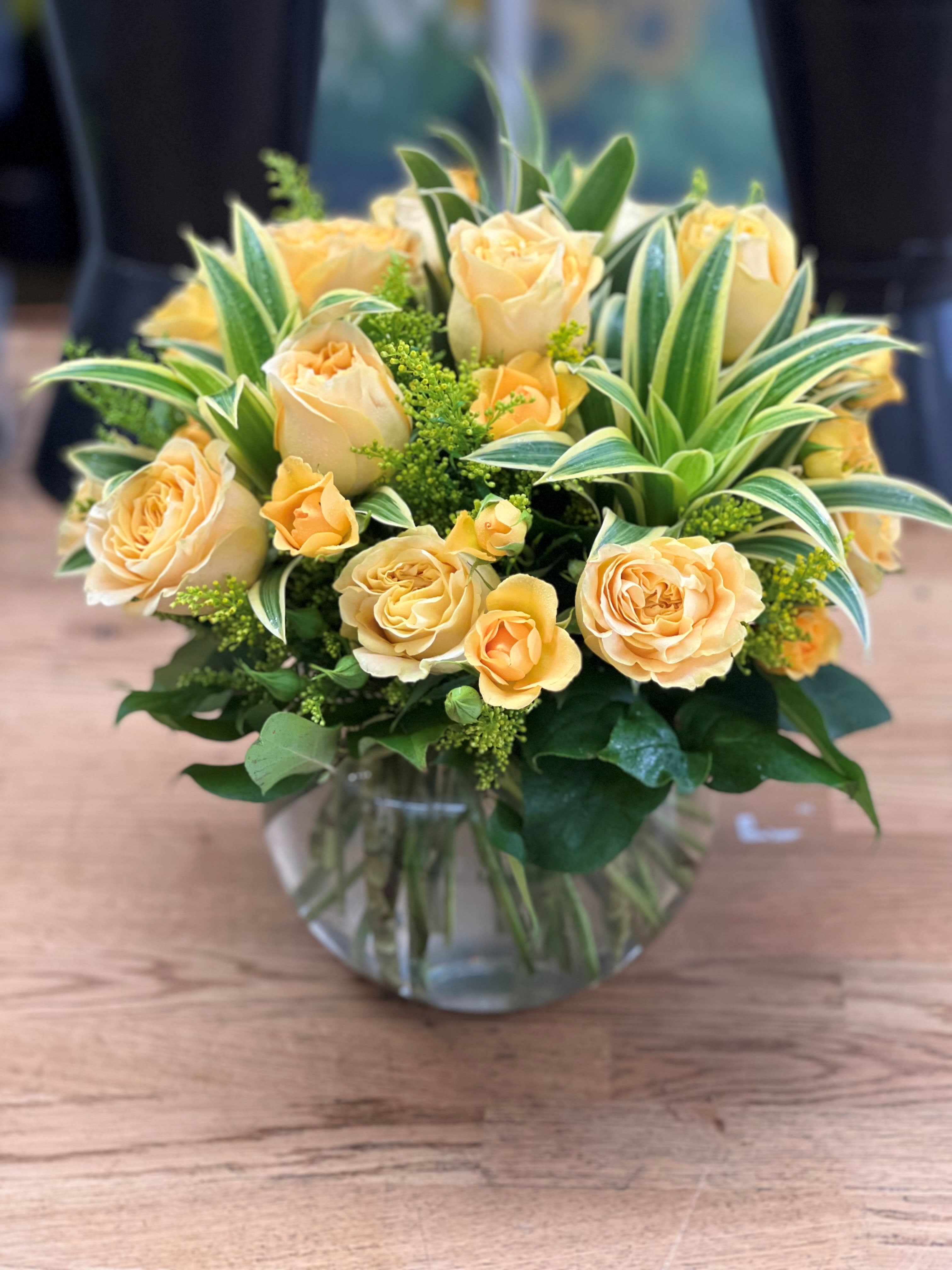 Peach roses in a clear glass vase with variegated foliage