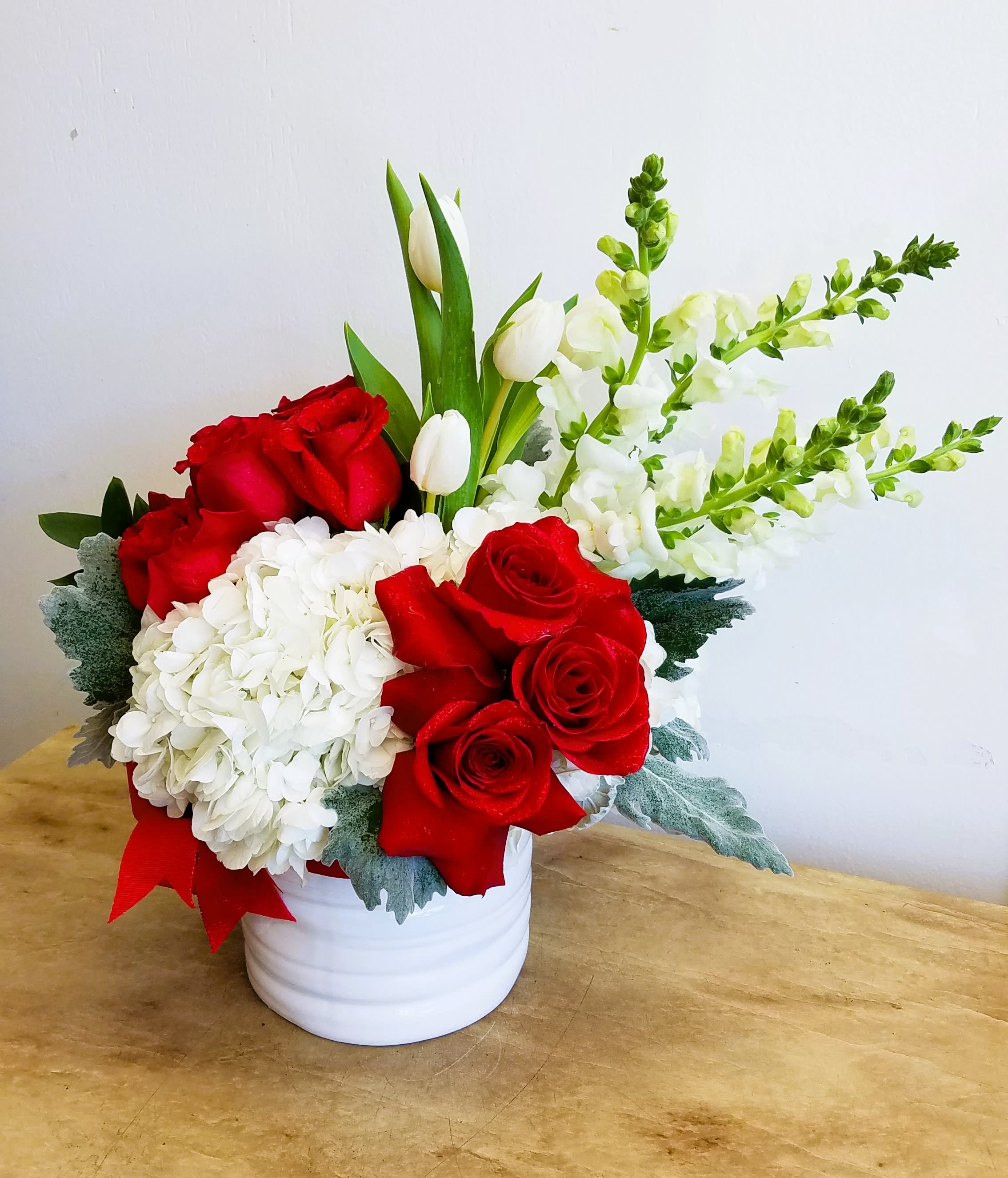 Red roses and white hydrangeas in a white vase with tulips and snapdragons
