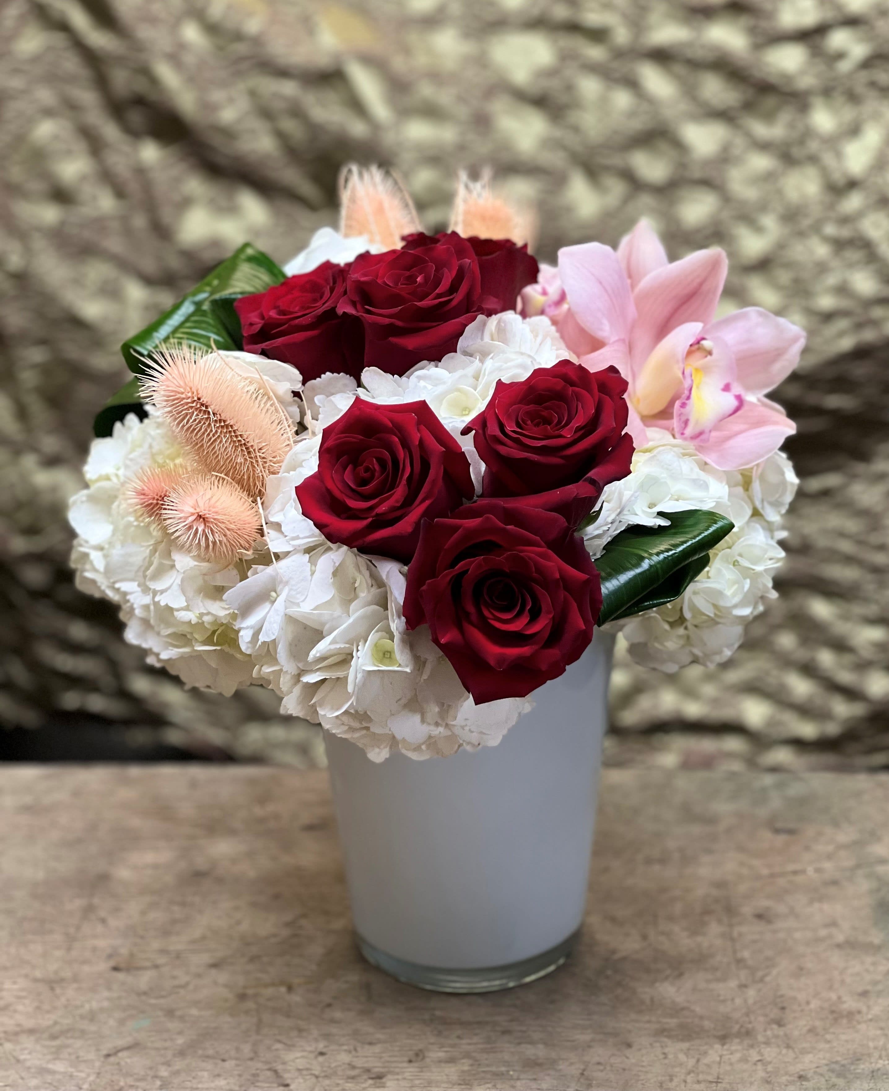 Red roses and white hydrangeas in a white vase with pink orchids