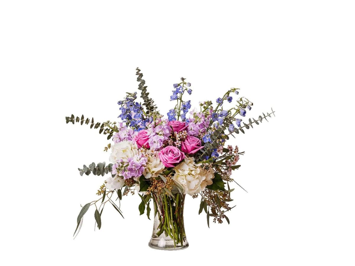Bouquet of pink roses, blue delphinium, and white hydrangeas in a glass vase