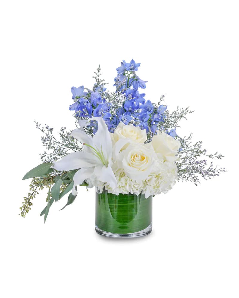 White lilies and roses in a glass vase with blue flowers