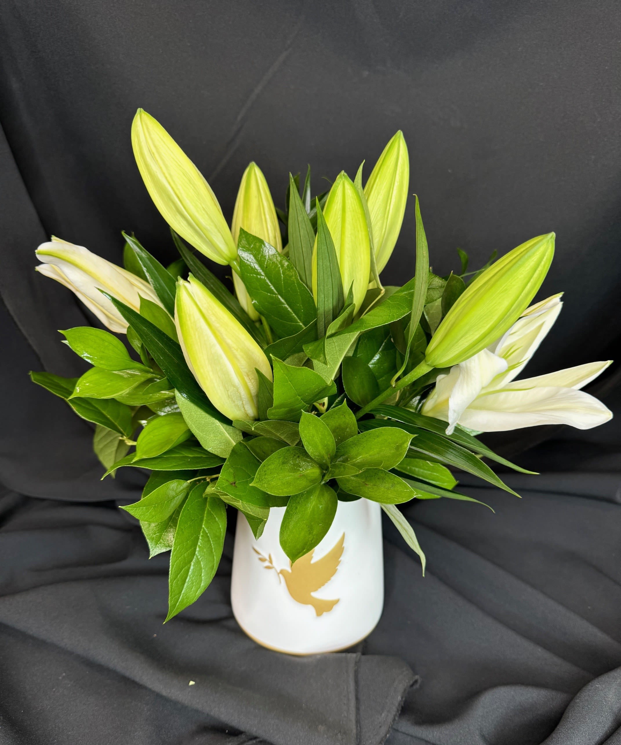 White lily buds in a white vase with a gold dove design