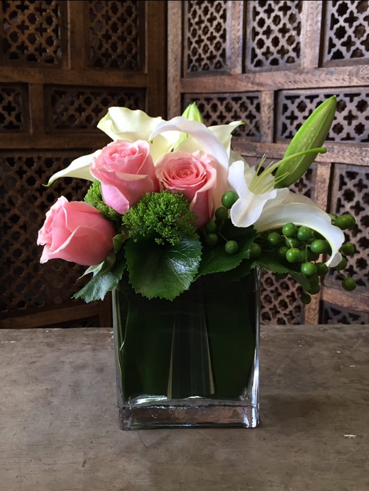 Pink roses and white lilies arranged in a square glass vase