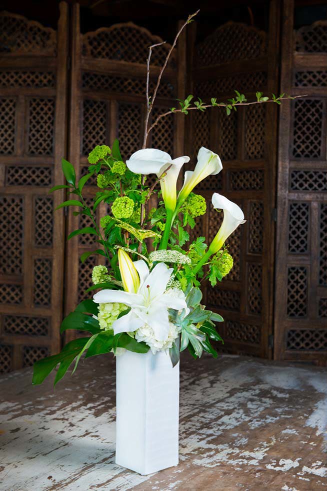 Tall white floral arrangement with calla lilies and lilies in a white vase