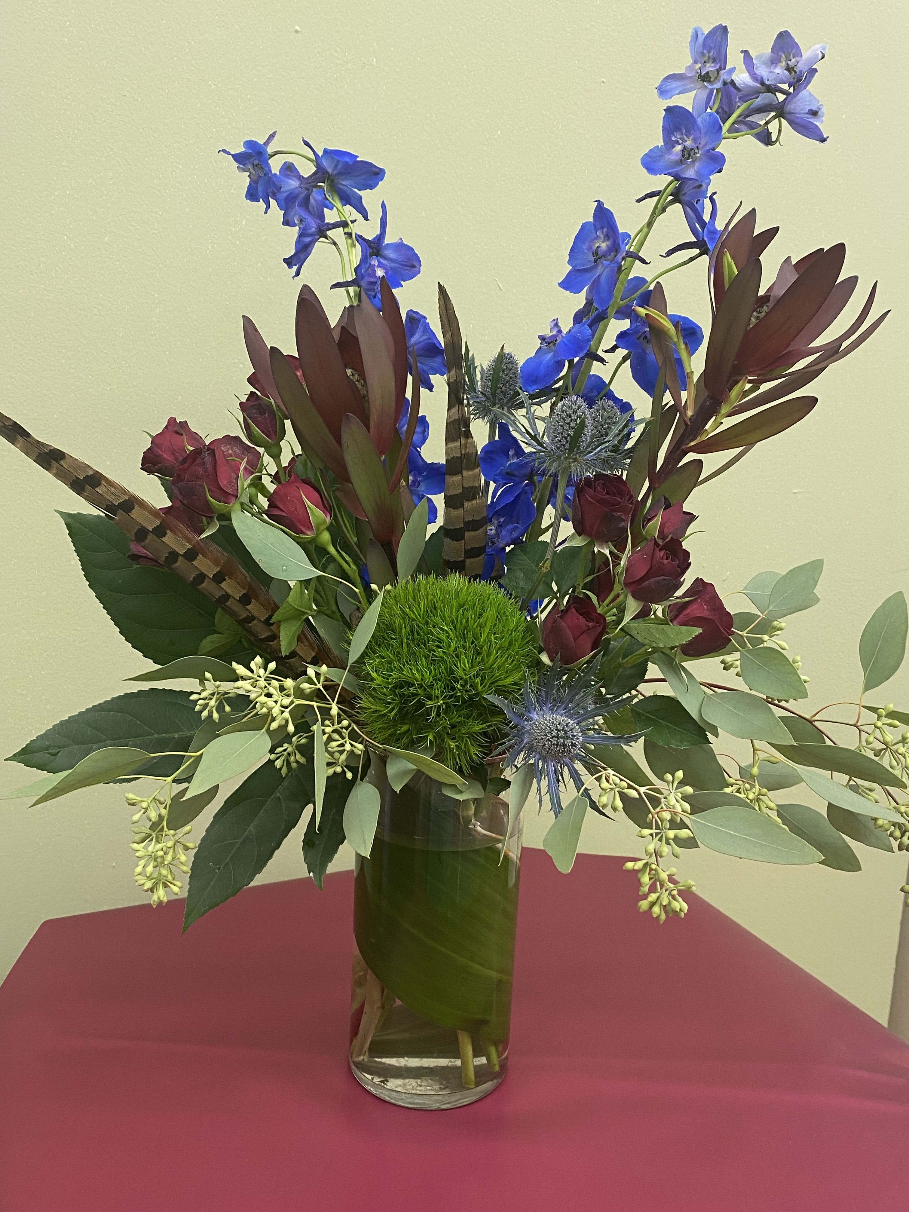 Tall vase arrangement with blue flowers, burgundy roses, and a green moss ball
