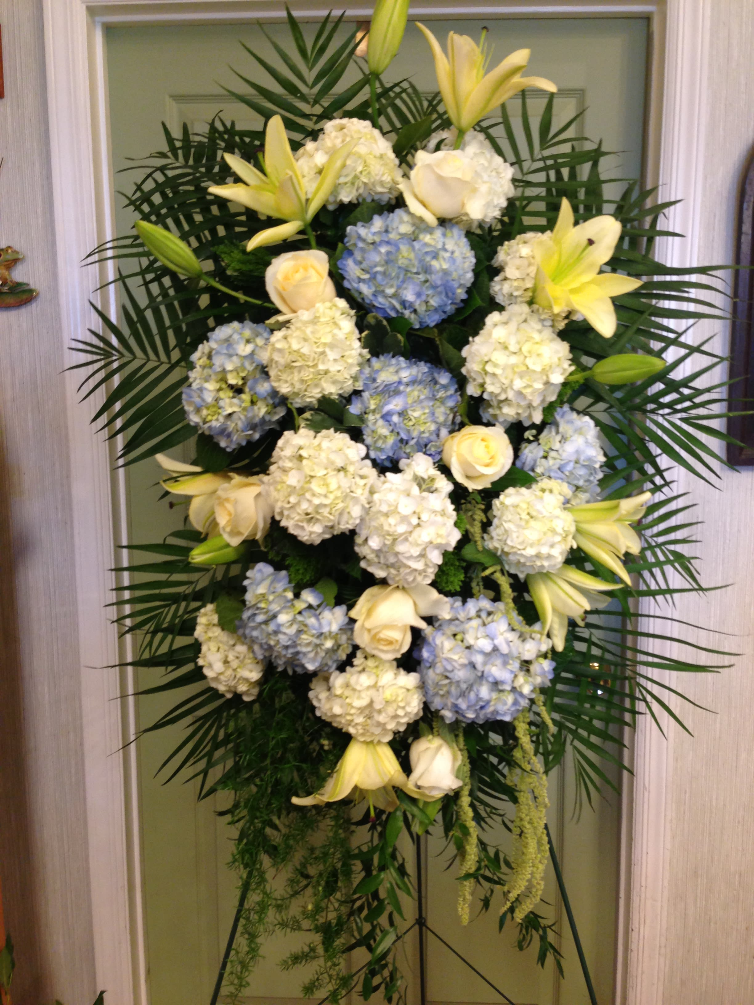 Tall standing floral spray with white lilies, roses, and blue hydrangeas