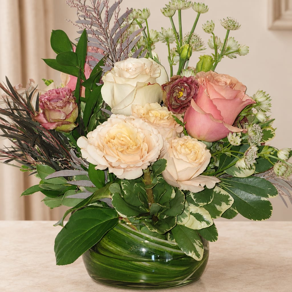 Pink and cream roses arranged in a green glass vase