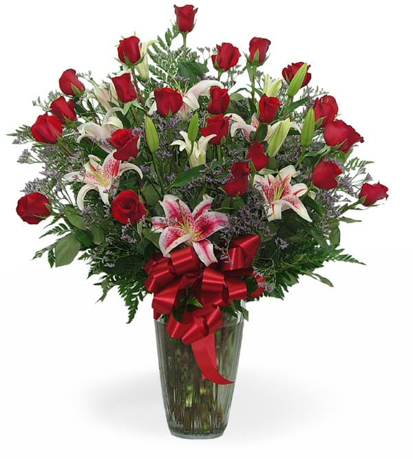 Bouquet of red roses and pink lilies in a glass vase with a red ribbon