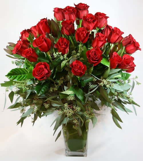 Red roses arranged in a clear glass vase with greenery